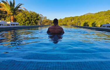 man in an infinity pool looking at the forest