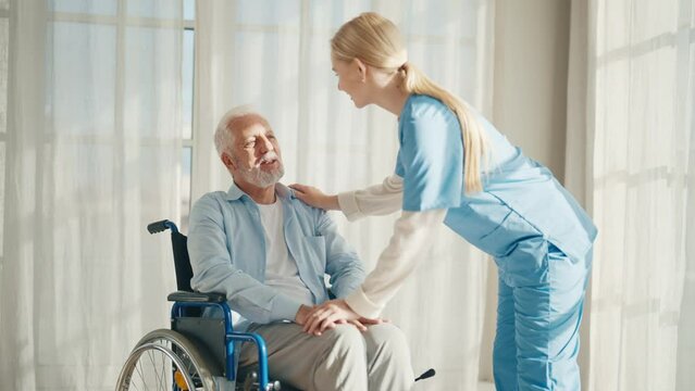 Caregiver in hospital helping an elderly patient for support in clinic. Medical nurse talking to a senior person with disability.Male person with a disability patient receives support and medical care