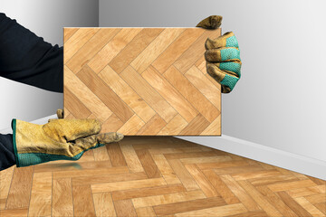Manual worker with protective work gloves holding a herringbone wood parquet sample, corner of a room with herringbone wooden parquet and white walls on background.