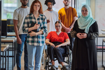 A diverse group of young business people walking a corridor in the glass-enclosed office of a modern startup, including a person in a wheelchair and a woman wearing a hijab, showing a dynamic mix of