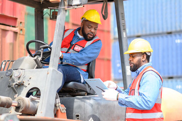 Two African American males in safety uniforms and helmets, container operating working with the forklift truck driver at commercial dock site. Cargo Ship Import Export Factory Logistic..
