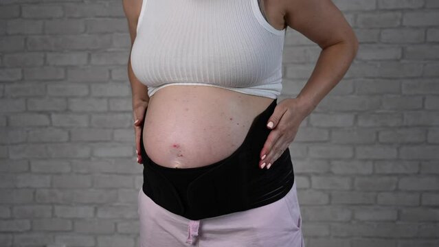 A pregnant woman puts on a black two-piece bandage. Cropped tummy. 
