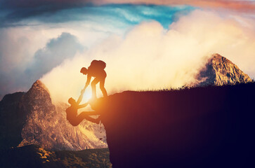 Man giving his hand to help his friend climb up the mountain - obrazy, fototapety, plakaty