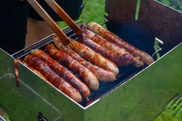 Person grillt Bratwürste auf einem Grill mit einer Grillzange