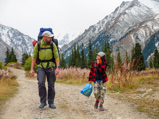 A man and a boy with backpacks walk along the road. Father and son walk in the mountains. Live communication between dad and child. Family time outdoors