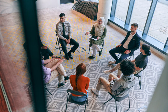 Top view of a diverse group of young business entrepreneurs gathered in a circle for a meeting, discussing corporate challenges and innovative solutions within the modern confines of a large