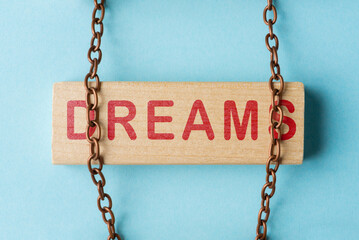 Wooden block with word Dreams is held by metal chain. Concept of realizing dreams and overcoming...