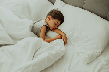 Calm little child sleeping well in comfortable bed. Boy in light cozy bedroom.