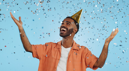 Man, birthday party hat and confetti in studio, smile or surprise for celebration by blue...