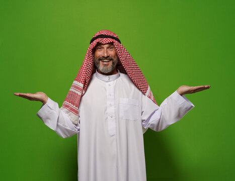 Muslim man holds two hands in gesture against green background, with empty blank copy space for text. Concept of choice and decision-making, man's contentment reflects satisfaction of making decision.