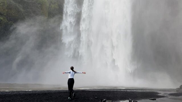 A girl spins around itself at a waterfall in Iceland