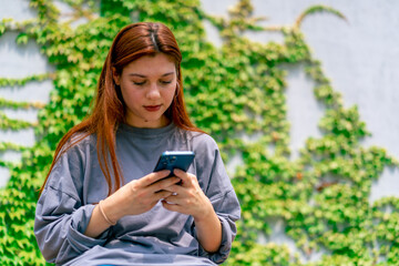 a young girl sits in the park on a bench with a phone in her hands chats with a friend on a social network reads the news