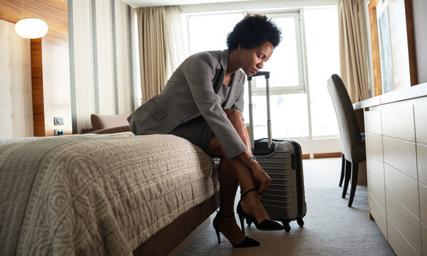 The businesswoman enters her hotel room, takes a seat onto the hotel bed. The comfort of the room offers a well-deserved moment after a long day of conferences and meetings.	
