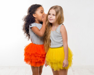 two little smiling girls with different complexion gossiping isolated on white background