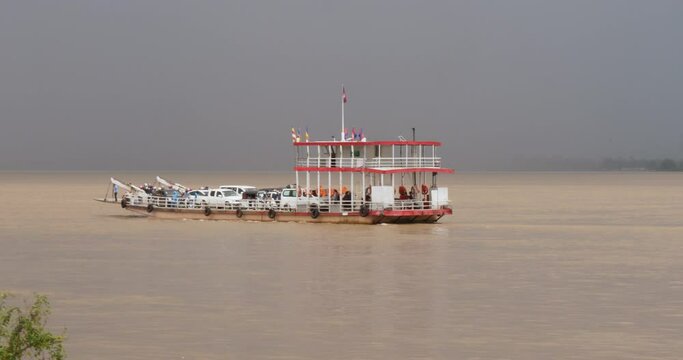 Ferry carrying cars and passengers on the Mekong River, with a dramatic sky in the background and a big rain approaching the boat.