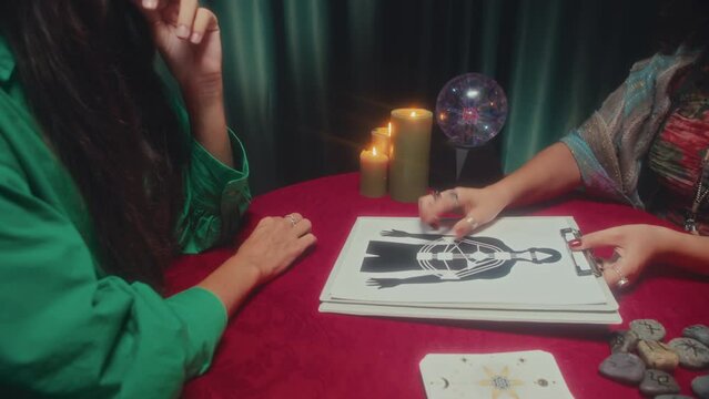 Medium shot of seer showing body chart to woman while sitting at table with burning candles during healing session
