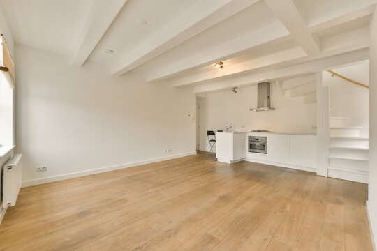 an empty living room with wood flooring and white painted walls in the corner to the kitchen is on the right