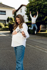 a pregnant woman holds an ultrasound picture in her hands, her husband jumps joyfully behind her. vertical photography. pregnant couple walking outside