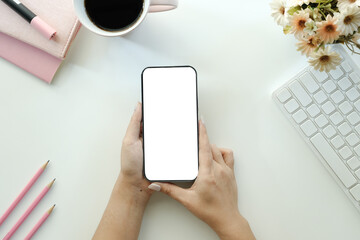 Cropped shot top view of businesswoman hands using smartphone mockup at the white office desk. Blank screen mobile phone for graphic display montage