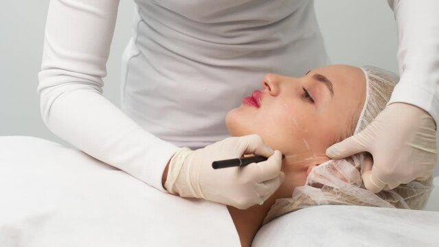 The cosmetologist makes markings on the patient's face, drawing correction lines before the facial contouring procedure or plastic surgery. preparation time for cosmetic treatment.
