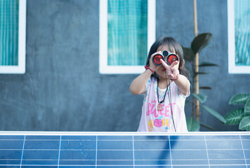 Happy Asian girl admiring solar panels with binoculars recently installed at home.