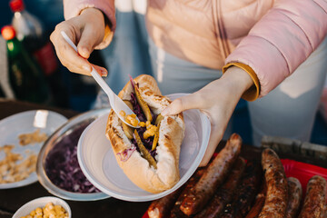 Woman cooking a delicious hotdog on a grill picnic outside. - obrazy, fototapety, plakaty