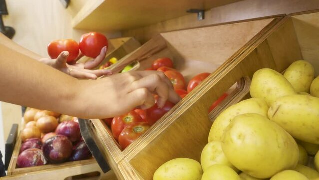 adding fresh products. young black woman putting tomatoes on shelf in supermarket. 
