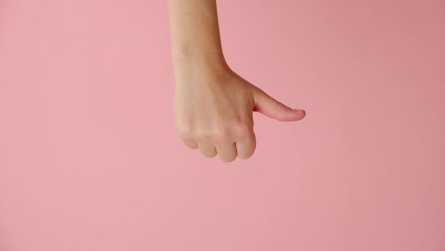Vertical footage of female hand showing thumb down, posing isolated over pink color background wall in studio with copy space for promotion content or design. Dislike and disapproval gesture concept