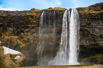 a waterfall on the side of a mountain that is under a blue sky
