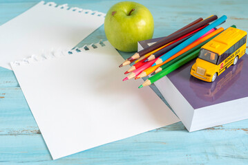 Colorful pencils, blank notebook paper, school bus toy over blue wooden background. Back to school...