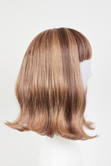 Naklejka premium Natural looking dark brunet wig on white mannequin head. Middle length brown hair on the plastic wig holder isolated on white background, side view.