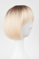 Naklejka premium Natural looking blonde fair wig on white mannequin head. Short hair cut on the plastic wig holder isolated on white background, side view.