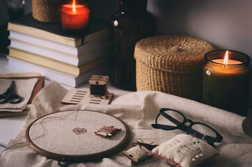 cross stitch embroidery in hoop with handcraft accessories and candles. Cozy evenings at home, hobby for winter and autumn season.