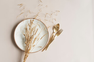 beige empty plate with golden cutlery on beige background with dried flowers bouquet. Boho minimalist aesthetic. Dishware mock up
