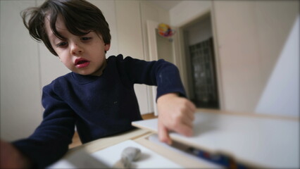 Creative Child preparing to draw, picking coloring pen from inside desk drawer, sititng down in bedroom concentrated to do school kindergarten study