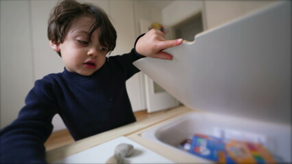 Creative Child preparing to draw, picking coloring pen from inside desk drawer, sititng down in...