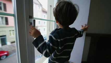 Fototapeta na wymiar Child holding into window knob. Danger concept of small boy near glass from second floor apartment residence