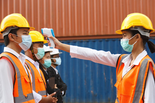asian man workers wearing face mask checking fever by digital thermometer before entering the work for protecting from illness pandemic or outbreak on construction site. selective focus. - Powered by Adobe