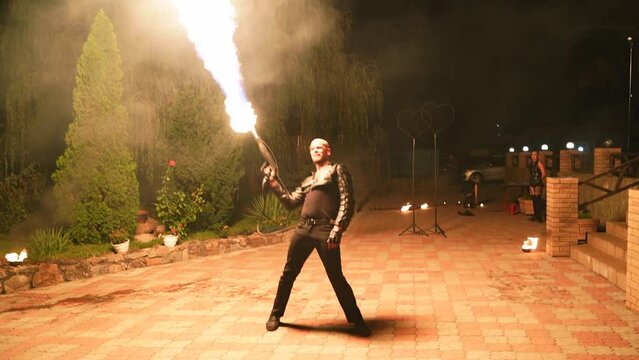 Fire performance show. Male artist performing with Flamethrower open air on the festival night. Fire dancer making show with flame outdoor at venue for tourists. Man working with fire on the street.