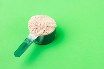 Chocolate whey protein powder in measuring spoon on green background. healthy eating, bodybuilding...