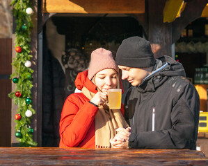 Happy girl and boy drinking hot mulled wine and smiling at Christmas market.