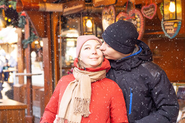 Boy kissing girl at the Christmas market. Happy pair in the front of the shop with gingerbread