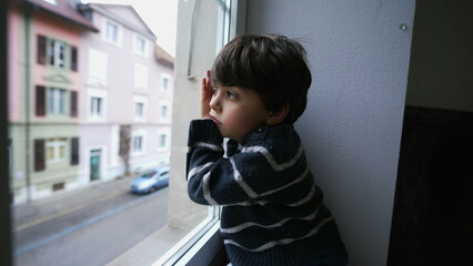 One bored child leaning on window looking out, little boy wanting to go outside. Sad depressed kid...