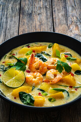 Thai soup with pumpkin, shrimps and coconut milk on wooden table
