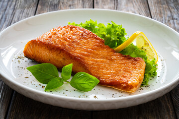 Seared salmon steak with lettuce and lemon on wooden table
