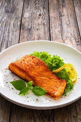 Seared salmon steak with lettuce and lemon on wooden table
