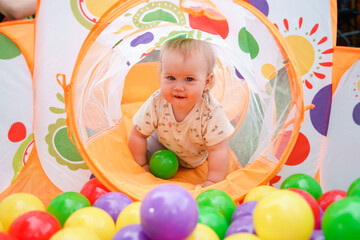 Fototapeta na wymiar The kid baby is having fun in a dry pool with balls. Having fun in playroom Leisure Activity.