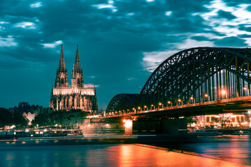 Cologne Cathedral and Hohenzollern Bridge in the evening with lighting against cloudy sky
