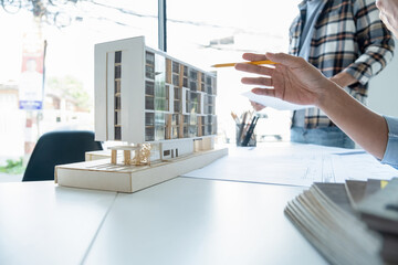 Engineers looking and discussing over blueprints and building model on desk.