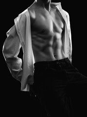Fototapeta premium Handsome sexy man with a pumped up body in a dark shirt on a black background. Sports and healthy lifestyle.